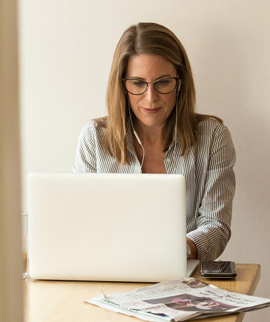 blonde woman wearing glasses sat at desk behind laptop